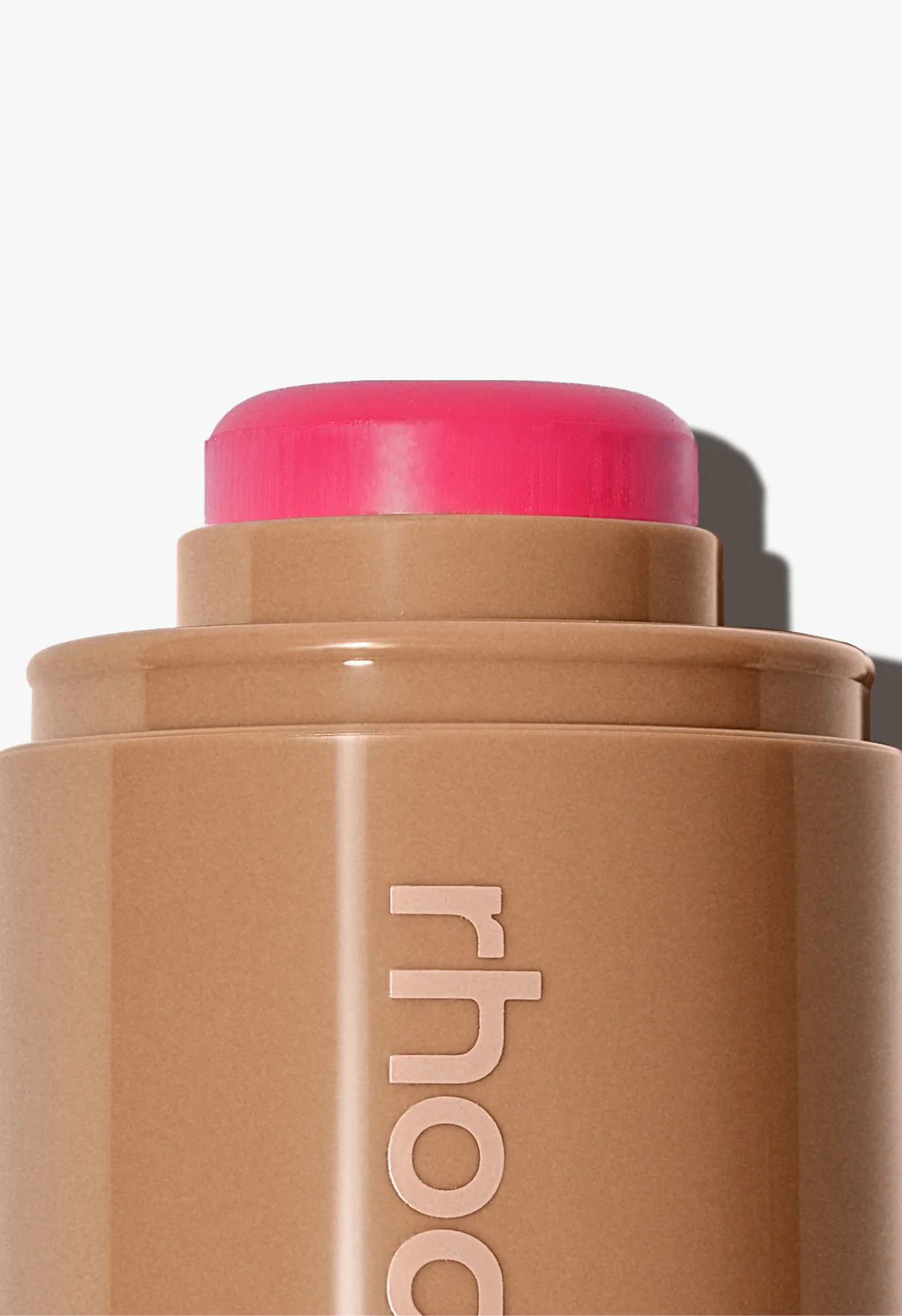 Cosmetic stick with pink cap and 'rhode' branding on a light background