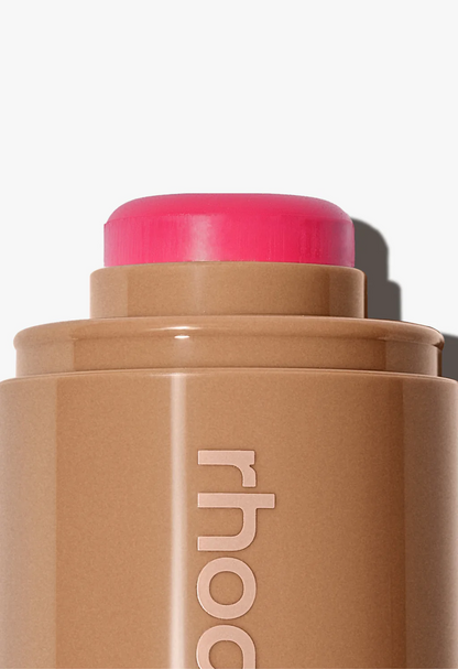 Cosmetic stick with pink cap and 'rhode' branding on a light background