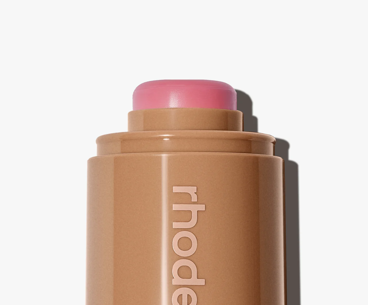Cosmetic stick with pink cap on a white background, featuring the brand 'rhode'.