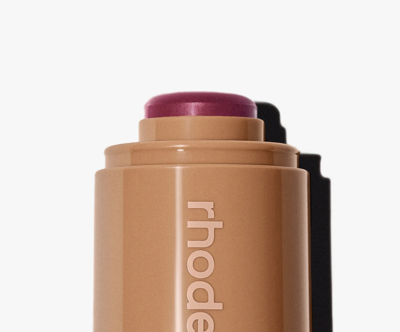 Cosmetic stick with purple top and 'rhode' branding on a white background